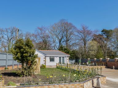A small white house with a gray roof surrounded by a garden with flowers and trees at Old Colliery Cottage in Shilbottle
