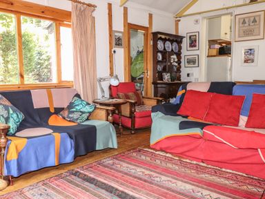A living room with sofas and cushions a wooden cabinet with plates and framed pictures on walls at Can Yr Afon in Beddgelert