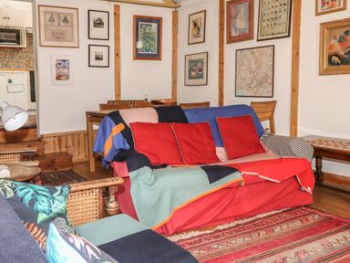 A living room with a sofa covered by colorful blankets and cushions a wooden table and chairs framed pictures on the wall at Can Yr Afon in Beddgelert