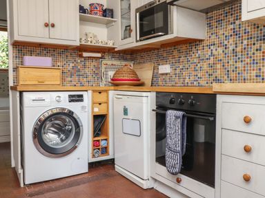 A kitchen with washing machine dishwasher oven microwave and tiled backsplash at Can Yr Afon in Beddgelert