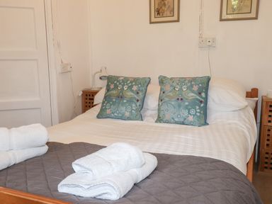 A bed with two blue pillows with bird designs white towels and bedside tables with lamps at Can Yr Afon in Beddgelert