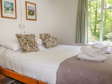 A bedroom with a made bed with floral pillows folded towels on a quilt near a window with checkered curtains at Can Yr Afon in Beddgelert