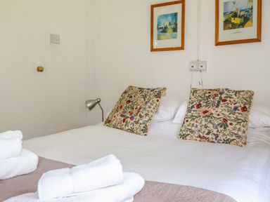 A bedroom with a double bed two floral pillows folded white towels a wall lamp and two framed pictures at Can Yr Afon in Beddgelert