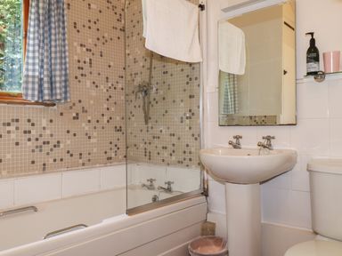 A bathroom with a bathtub shower combination a sink toilet and a window with checkered curtains at Can Yr Afon in Beddgelert