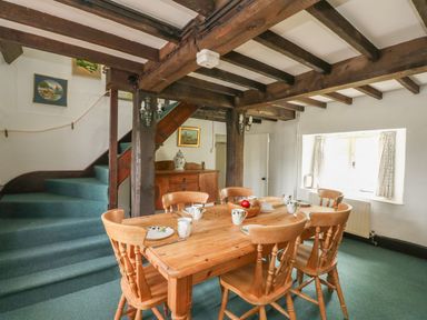 A dining area with wooden table and chairs near stairs and window at Thatch Cottage in Buckland Newton