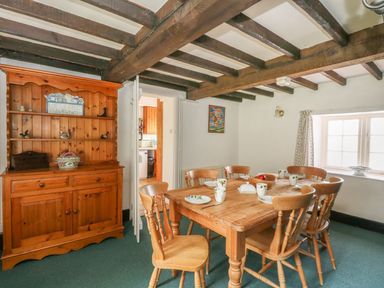 A dining room with wooden table and chairs a wooden cabinet and a window at Thatch Cottage in Buckland Newton