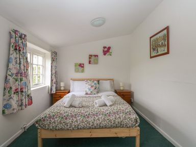 A bedroom with a double bed floral bedding bedside tables lamps and floral curtains at Thatch Cottage in Buckland Newton