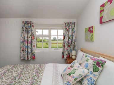 A bedroom with a bed covered in floral bedding beside a window with floral curtains at Thatch Cottage in Buckland Newton