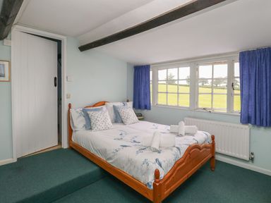 A bedroom with a wooden double bed and blue curtains by the windows at Thatch Cottage in Buckland Newton
