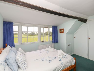 A bedroom with a wooden bed and floral bedding next to large windows with blue curtains at Thatch Cottage in Buckland Newton