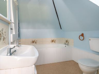 A bathroom with a sink a bathtub with floral tiles and a toilet at Thatch Cottage in Buckland Newton