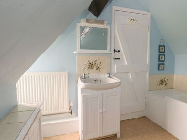 A bathroom with a sink cabinet radiator door and bathtub with blue walls at Thatch Cottage in Buckland Newton