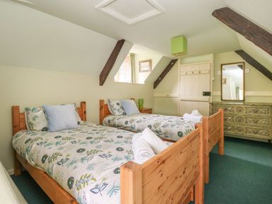 A bedroom with two single beds floral bedding wooden furniture and a dresser at Thatch Cottage in Buckland Newton