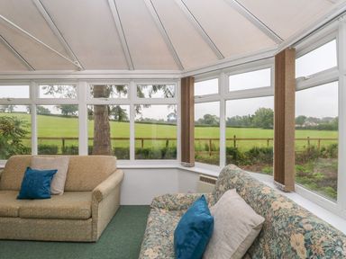 A conservatory with two sofas and cushions overlooking a green field at Thatch Cottage in Buckland Newton