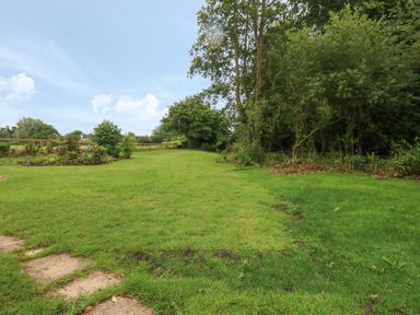 A garden area with grass and trees along the side at Thatch Cottage in Buckland Newton