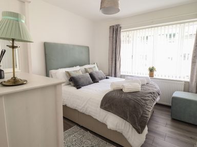 A bedroom with a bed with pillows and blankets a dresser with a lamp and a window with curtains at The Old Coach House in Conwy