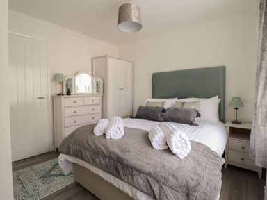 A bedroom with a bed with rolled towels a wardrobe a chest of drawers and a bedside table at The Old Coach House in Conwy