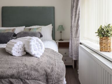 A bedroom with a bed with pillows and rolled towels a bedside table with a lamp and a window with a potted plant at The Old Coach House in Conwy