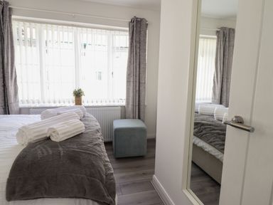 A bedroom with a bed covered in white and gray bedding with rolled white towels on top near a window with vertical blinds and gray curtains at The Old Coach House in Conwy