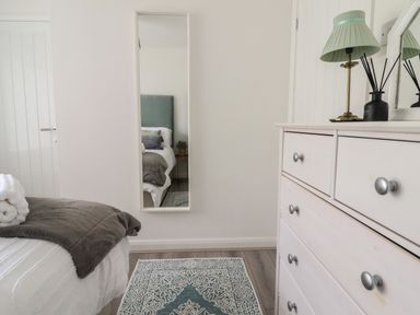 A bedroom with a white dresser with a green lamp and a mirror on the wall at The Old Coach House in Conwy