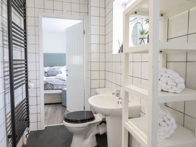 A bathroom with a toilet, sink, white shelving unit with towels, and a black heated towel rail at The Old Coach House in Conwy