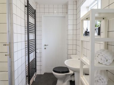 A bathroom with a toilet a sink a shelf with towels and a radiator at The Old Coach House in Conwy
