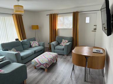 A living room with two sofas an armchair an ottoman a dining table and chairs a floor lamp and a wall-mounted television at The Old Coach House in Conwy