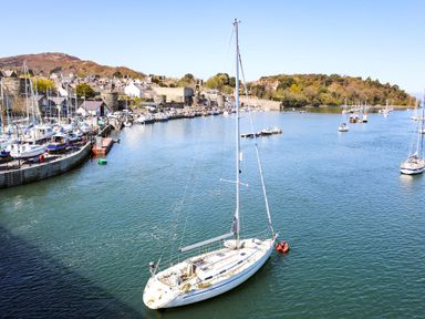 A harbor with sailboats and yachts on the water near a town with stone buildings and hills in the background at The Old Coach House in Conwy