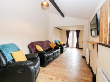 A living room with black recliner sofas yellow and blue cushions and a wall mounted television at Squirrel Lodge in North Walsham