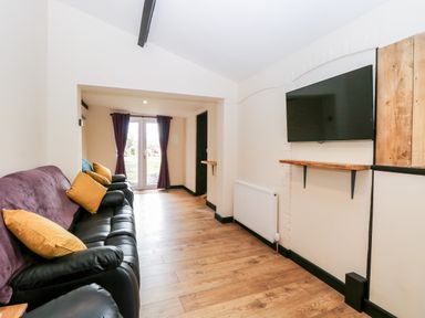 A living room with black leather sofas yellow pillows mounted television and wooden floor at Squirrel Lodge in North Walsham