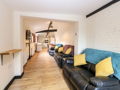 A living room with black leather sofas and yellow cushions leading to a kitchen and dining area at Squirrel Lodge in North Walsham