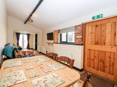 A dining and living area with a wooden table and chairs a door a television and a window at Squirrel Lodge in North Walsham