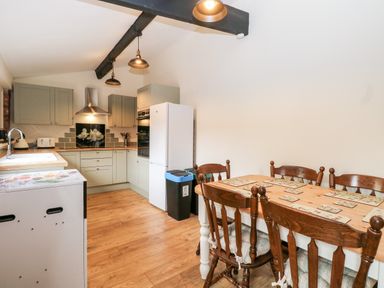 A kitchen with wooden floor wooden dining table with chairs and light green cabinets at Squirrel Lodge in North Walsham