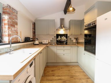 A kitchen with gray cabinets wooden countertops a washing machine and a white refrigerator at Squirrel Lodge in North Walsham