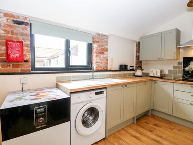 A kitchen with washing machine kettle toaster and green cabinets at Squirrel Lodge in North Walsham