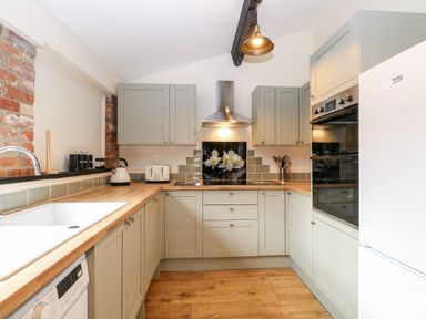 A kitchen with wooden countertops grey cabinets stainless steel oven and hood and a white fridge at Squirrel Lodge in North Walsham