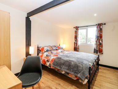 A bedroom with a bed next to a window with patterned curtains and a black chair at Squirrel Lodge in North Walsham