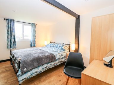 A bedroom with a bed a black chair and a desk with a mirror at Squirrel Lodge in North Walsham