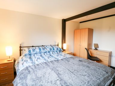 A bedroom with a double bed lamps on bedside tables wardrobe and a dresser with a chair at Squirrel Lodge in North Walsham