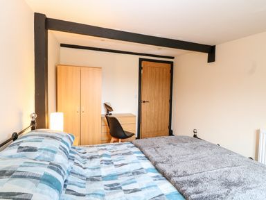 A bedroom with a bed with blue patterned bedding a wooden wardrobe desk black chair and wooden door at Squirrel Lodge in North Walsham