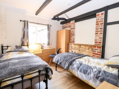 A bedroom with two single beds a wooden wardrobe a chest of drawers and a window with curtains at Squirrel Lodge in North Walsham