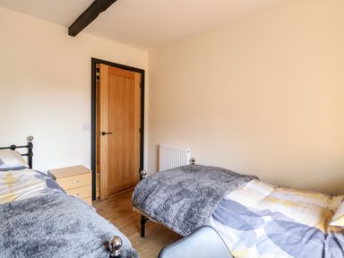 A bedroom with two single beds wooden floor a door and a wooden drawer unit at Squirrel Lodge in North Walsham