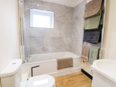 A bathroom with a bathtub shower combination toilet towel rack with multiple towels and wooden floor at Squirrel Lodge in North Walsham