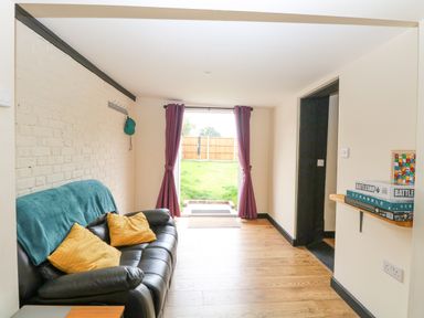 A sitting room with a black sofa yellow cushions and an open door leading to a garden at Squirrel Lodge in North Walsham