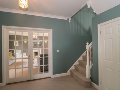 A hallway with turquoise walls carpeted stairs and glass paneled double doors leading to a living room at Cherry Tree House in Highbridge