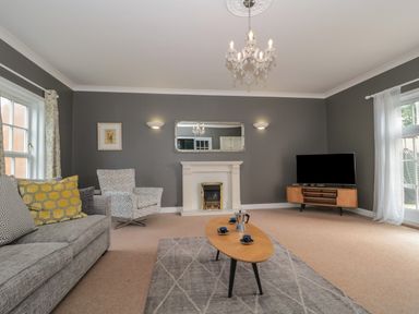 A living room with a sofa chairs a coffee table a fireplace a TV on a stand and windows at Cherry Tree House in Highbridge