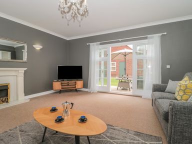 A living room with a gray sofa a wooden coffee table with cups a television on a stand and glass doors leading to a garden at Cherry Tree House in Highbridge