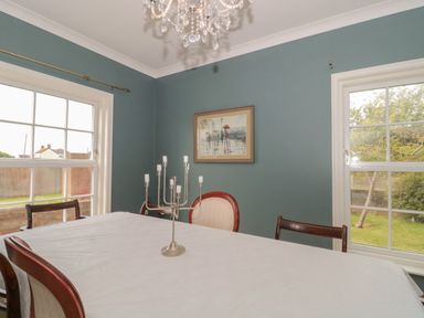 A dining room with a table covered by a white tablecloth and a silver candle holder between two windows at Cherry Tree House in Highbridge