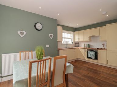 A kitchen with cream cabinets wooden floor and a dining table with chairs at Cherry Tree House in Highbridge