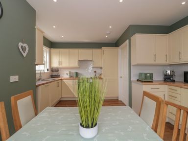 A kitchen with cream cabinets green walls a table with a potted plant and wooden chairs at Cherry Tree House in Highbridge